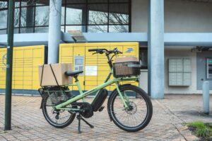Elektrisches Lastenrad mit Paketen vor Postschließfächern - Klimafreundliche Lieferung im Handwerk