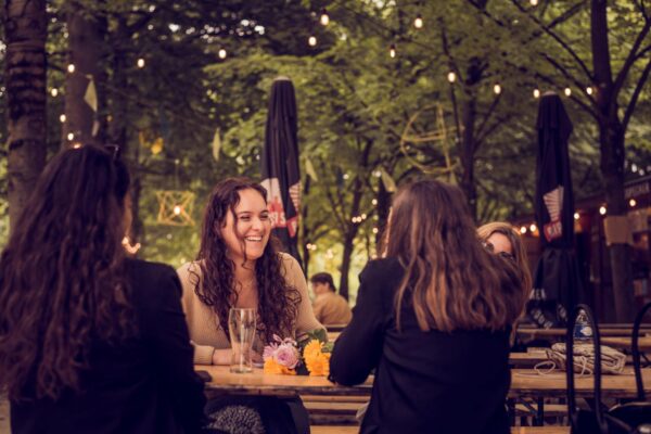 Menschen sitzen gemeinsam an einem Tisch im Biergarten als Symbolbild fuer schoenster Biergarten Muenchen