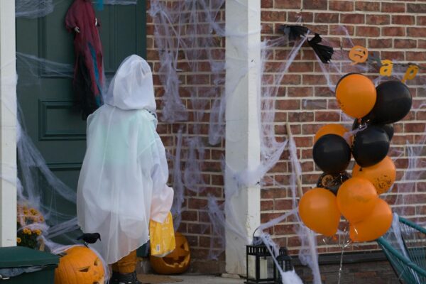 Kind im Geisterkostuem vor einer mit Kuerbissen geschmueckten Halloween-Tuer als Symbolbild fuer Halloween Bayern