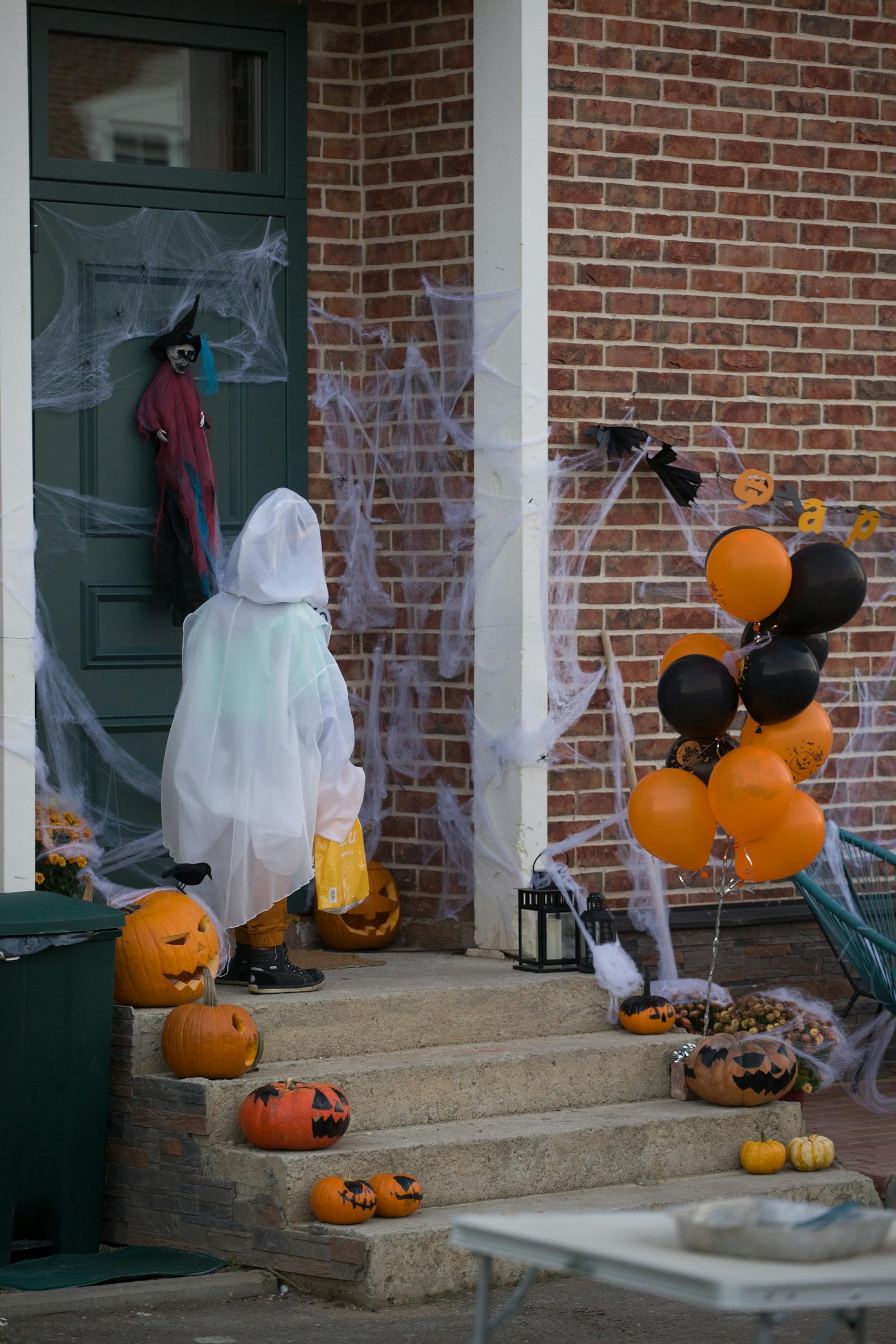 Kind im Geisterkostuem vor einer mit Kuerbissen geschmueckten Halloween-Tuer als Symbolbild fuer Halloween Bayern